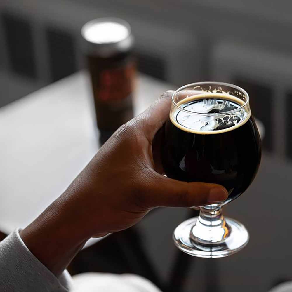A close up photo of a hand holding a glass of dark craft beer, a baltic porter