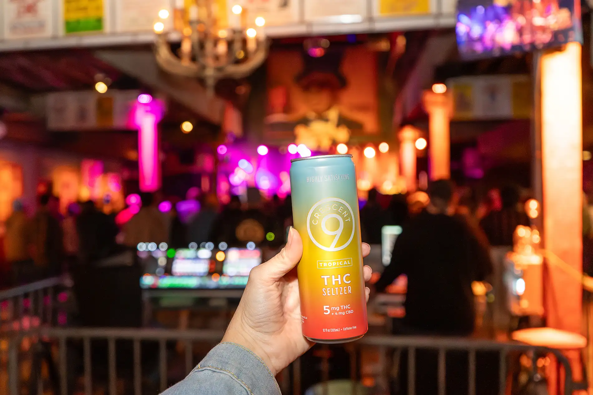 A hand holding a Crescent Canna THC beverage can in a night club like environment