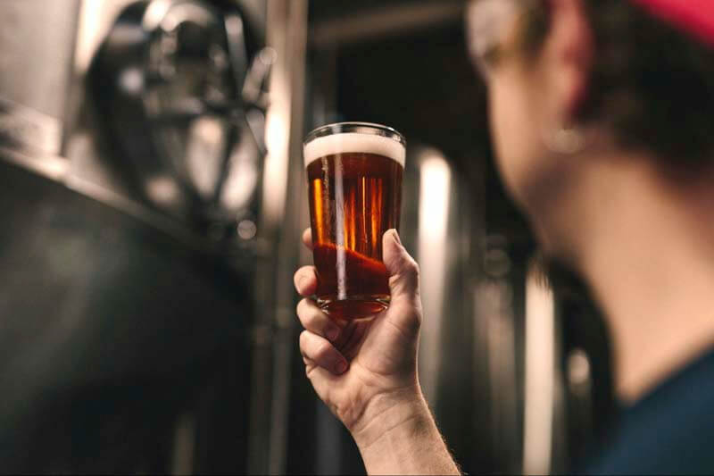 A close up photo of a brewer inspecting a freshly brewed pint of beer from their tank