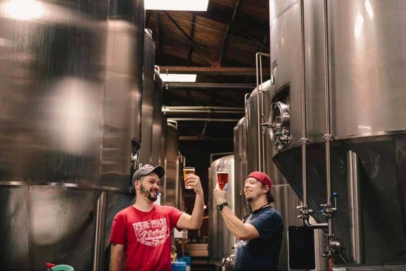 Two brewers inspecting freshly brewed beer in front of tanks