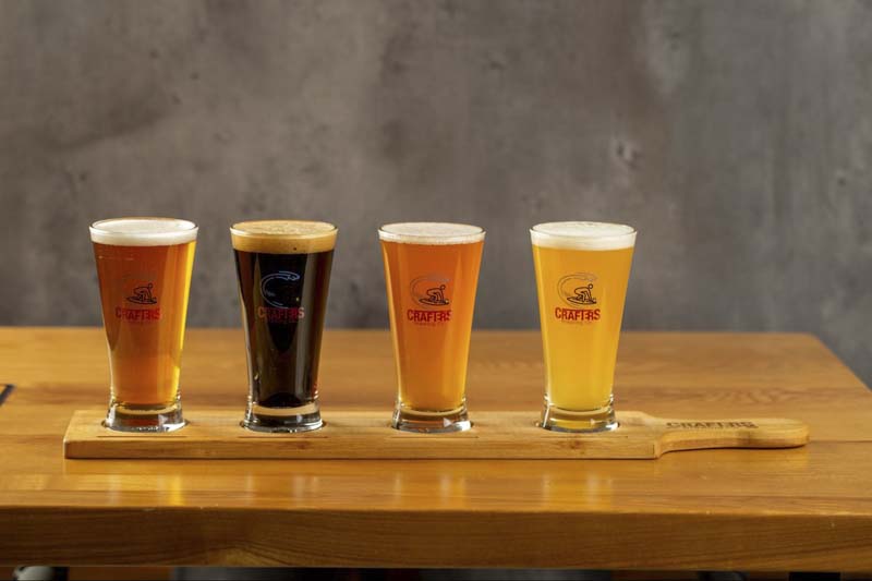A flight of various beers served in branded glassware