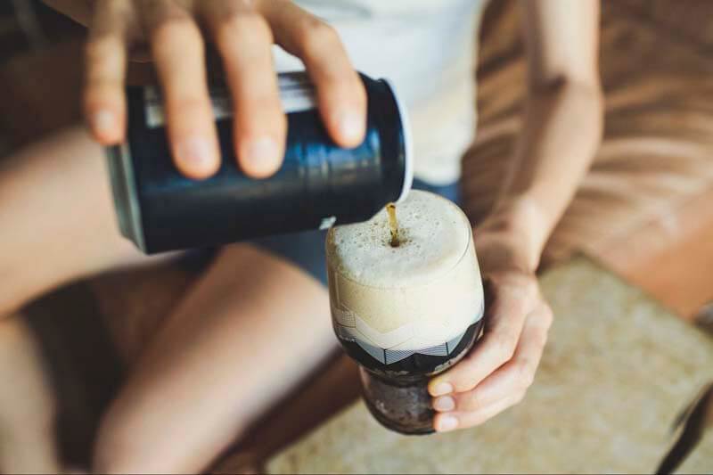 A close-up photo of a person pouring a non-alcoholic beer into a glass
