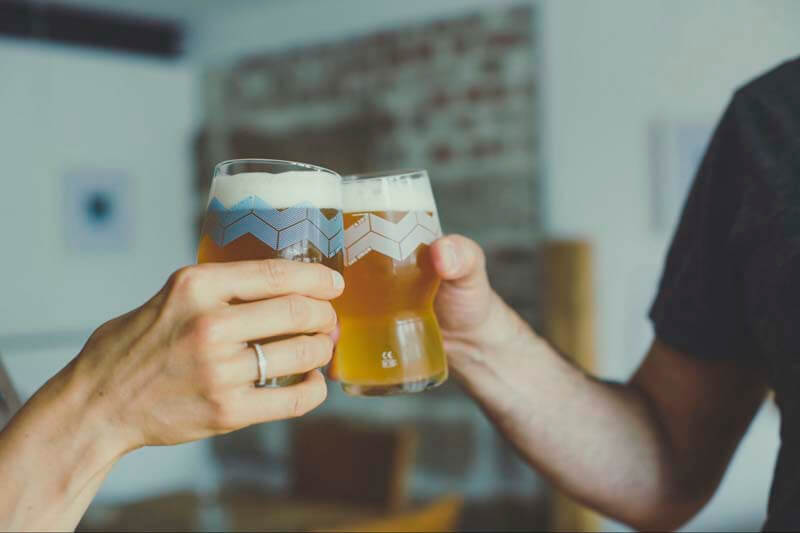 A close-up photo of two people toasting non-alcoholic beer in glasses