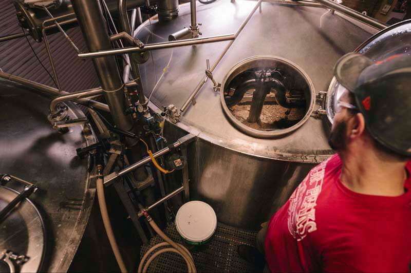 An overhead photo of a brewer lookign down into a tank during a non-alcoholic brewing process