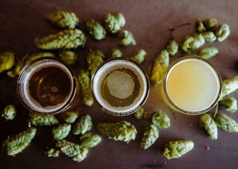 Overhead shot of three different varieties of beer in glass mixed with hops on a wooden table