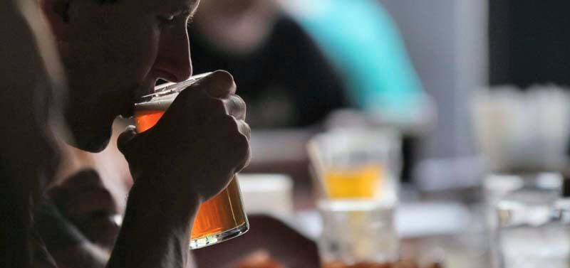 Side profile photo of a person enjoying a non-alcoholic beer from a glass while sitting at a busy bar