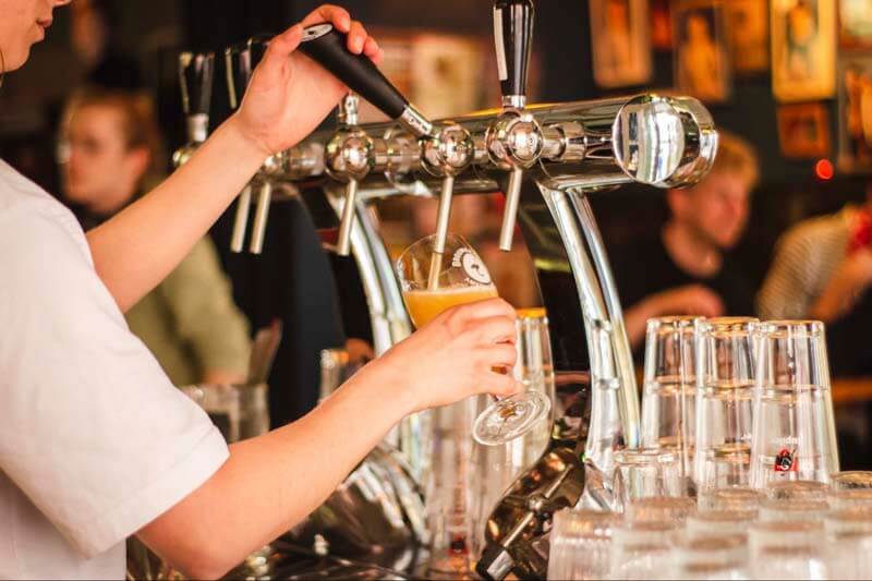 Photo of a bartender pouring beer into a glass from a tap