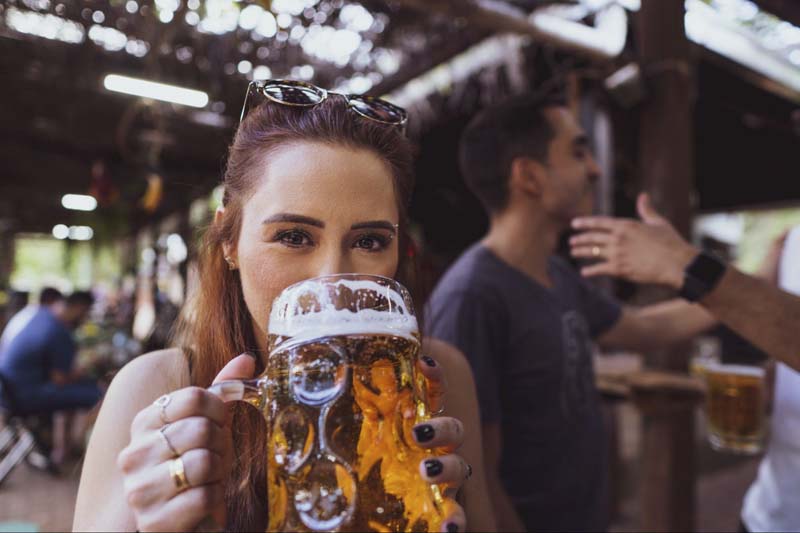 A woman drinking out of a large, non-branded glass beer mug at a brewery or bar