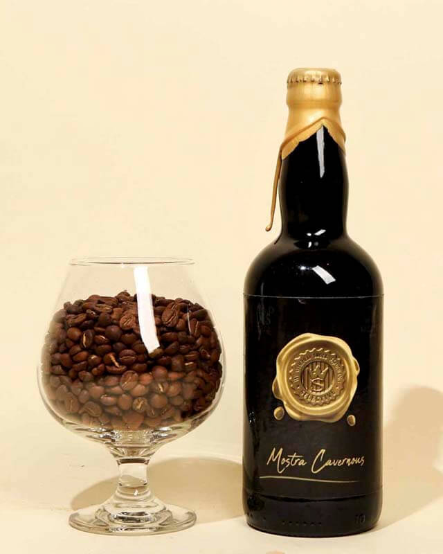 A bottle of coffee beer next to a beer glass filled with roasted coffee beans
