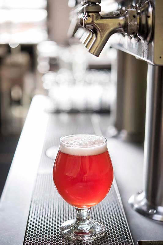 A bright colored craft beer made with fruit purees poured directly from a tap at a bar