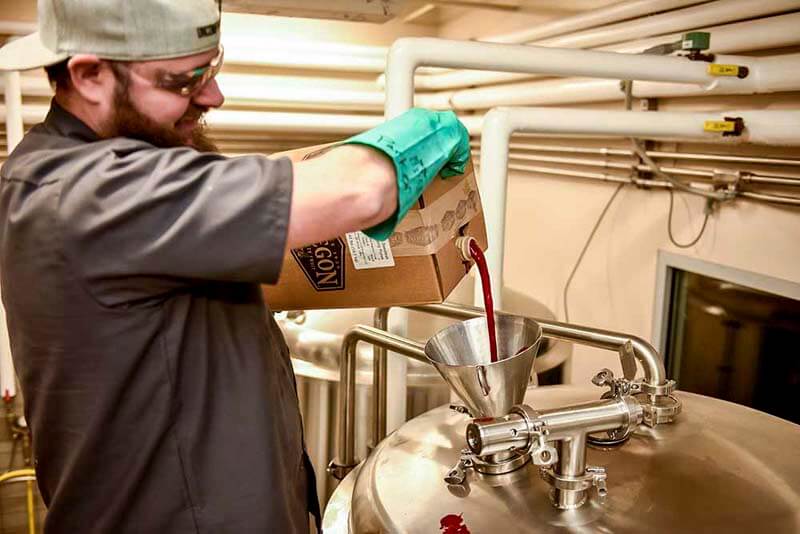 A brewer pouring fruit puree from Oregon Fruit Products into a fermentation tank during the craft beer brewing process