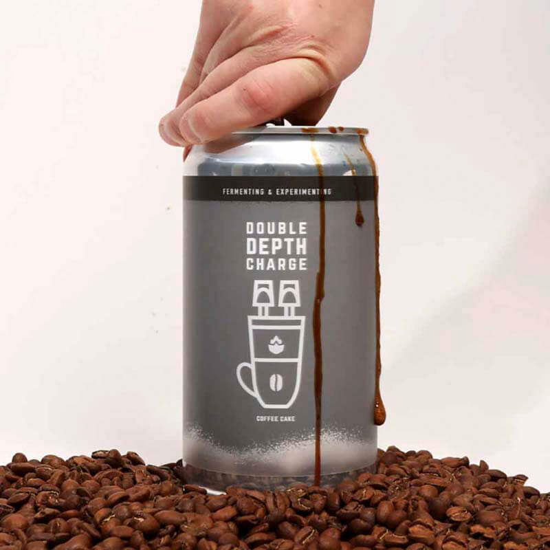 A can of Double Depth Charge coffee beer being opened among a pile of coffee beans on a table