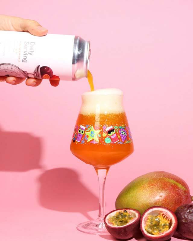 A can of Daily Serving craft beer made using fruit purees being poured into a beer glass with artwork