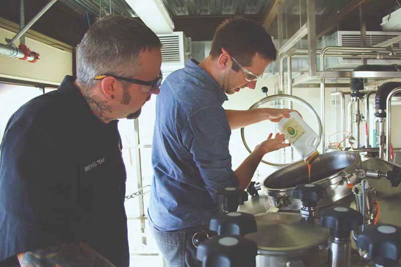 Two brewers pouring Incognito hop product into a craft brewery tank
