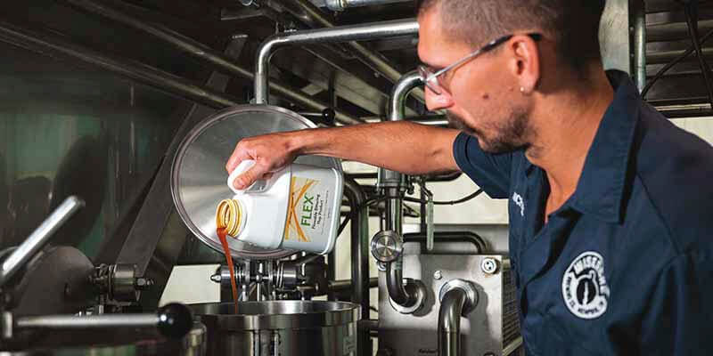 A photo of a brewer pouring FLEX alpha acid hop extract into a beer tank at a craft brewery