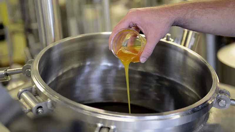 A close up of a hand pouring FLEX alpha acid hop extract into a container from a smaller cup
