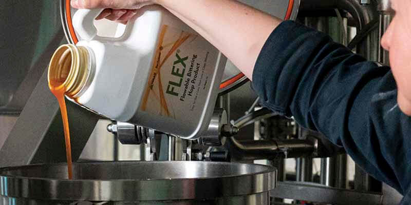 A close up photo of a brewer pouring FLEX alpha acid hop extract into a tank