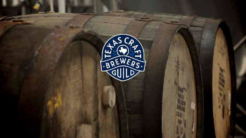 The Texas Craft Brewers Guild crest and logo on an image of barrels
