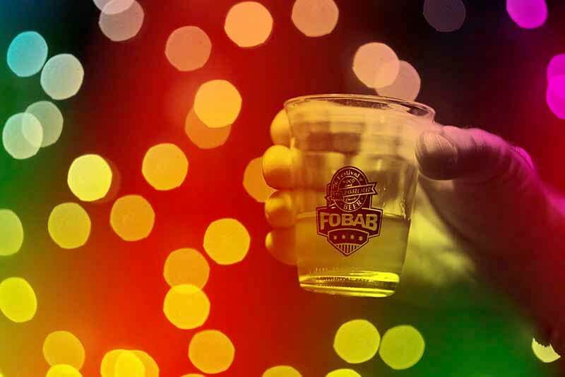 A bokeh light photo of a hand holding a Festival of Barrel-Aged Beers commemorative glass