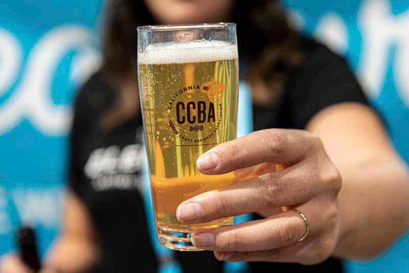 An outstretched hand presenting a CCBA branded beer glass filled with local craft beer