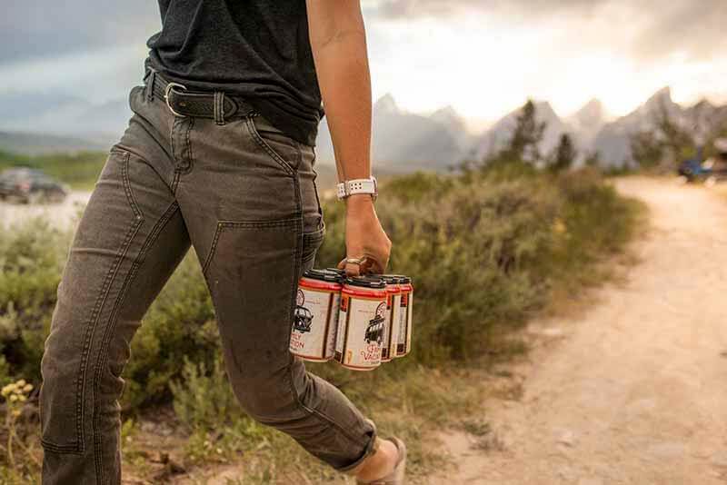 A person walking down a road carrying a six-pack of Roadhouse Brewing Co. craft beer