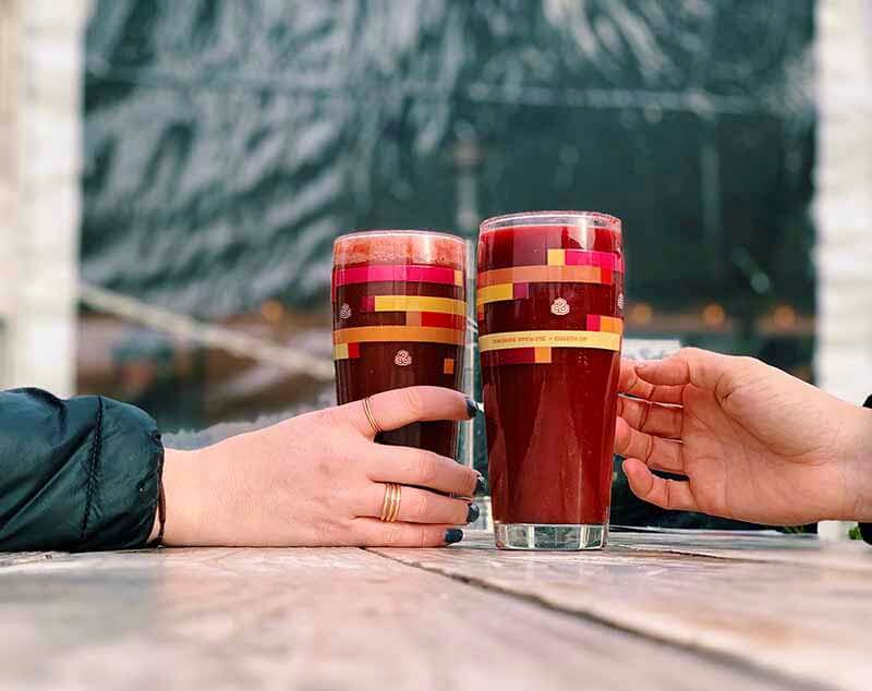 Two hands reaching for two glasses of red colored or berry-based sour smoothie beers at Oakshire Brewing