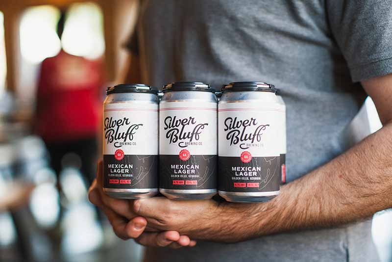Promotion photo of a person holding a six pack of Silver Bluffs Brewing Co. Mexican Style lager