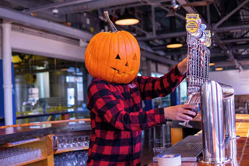 A brewer at Two Roads Brewing tending bar with a pumpkin on their head