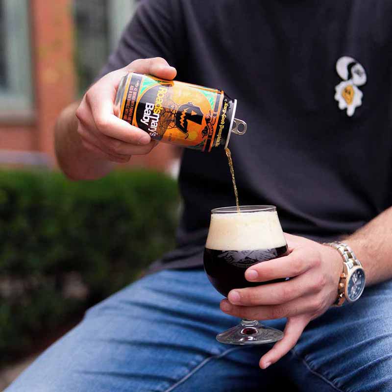 A promotinoal photo of a person pouring a can of Roadsmary's Baby pumpkin flavored craft beer into a glass