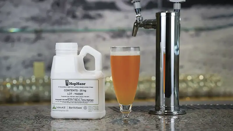 A container of Hop Haze sitting on a bar counter with a beer tap and beer glass