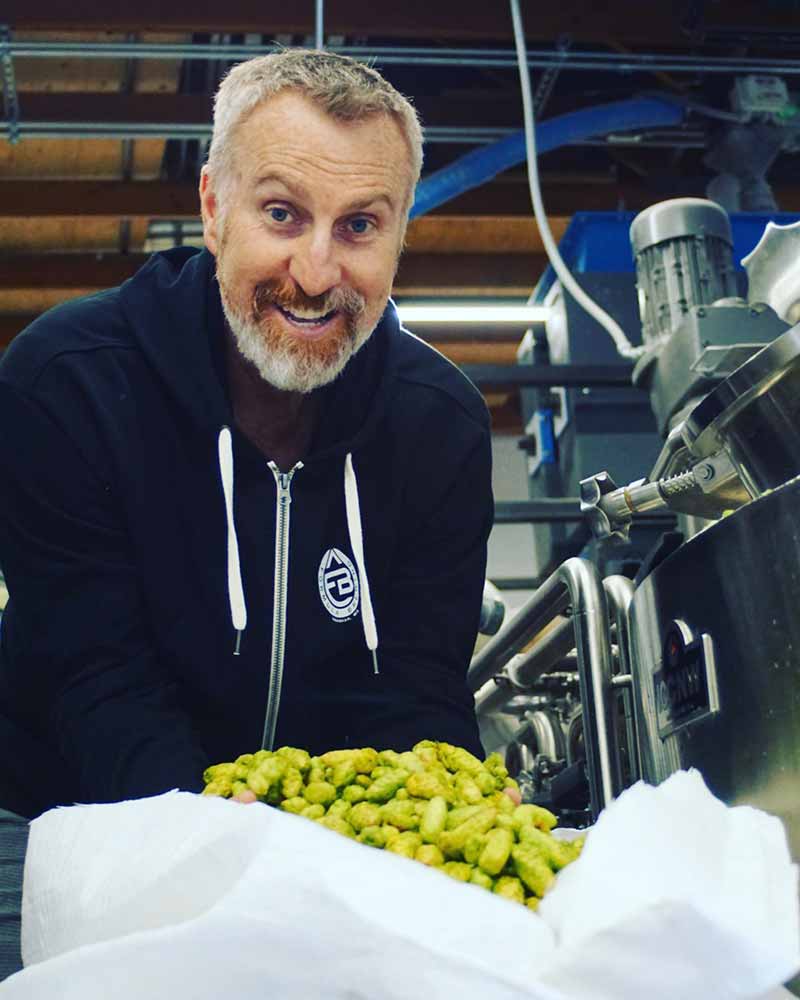 A brewer at Formula Beers smiles as he holds a pile of fresh hops in a brewery setting